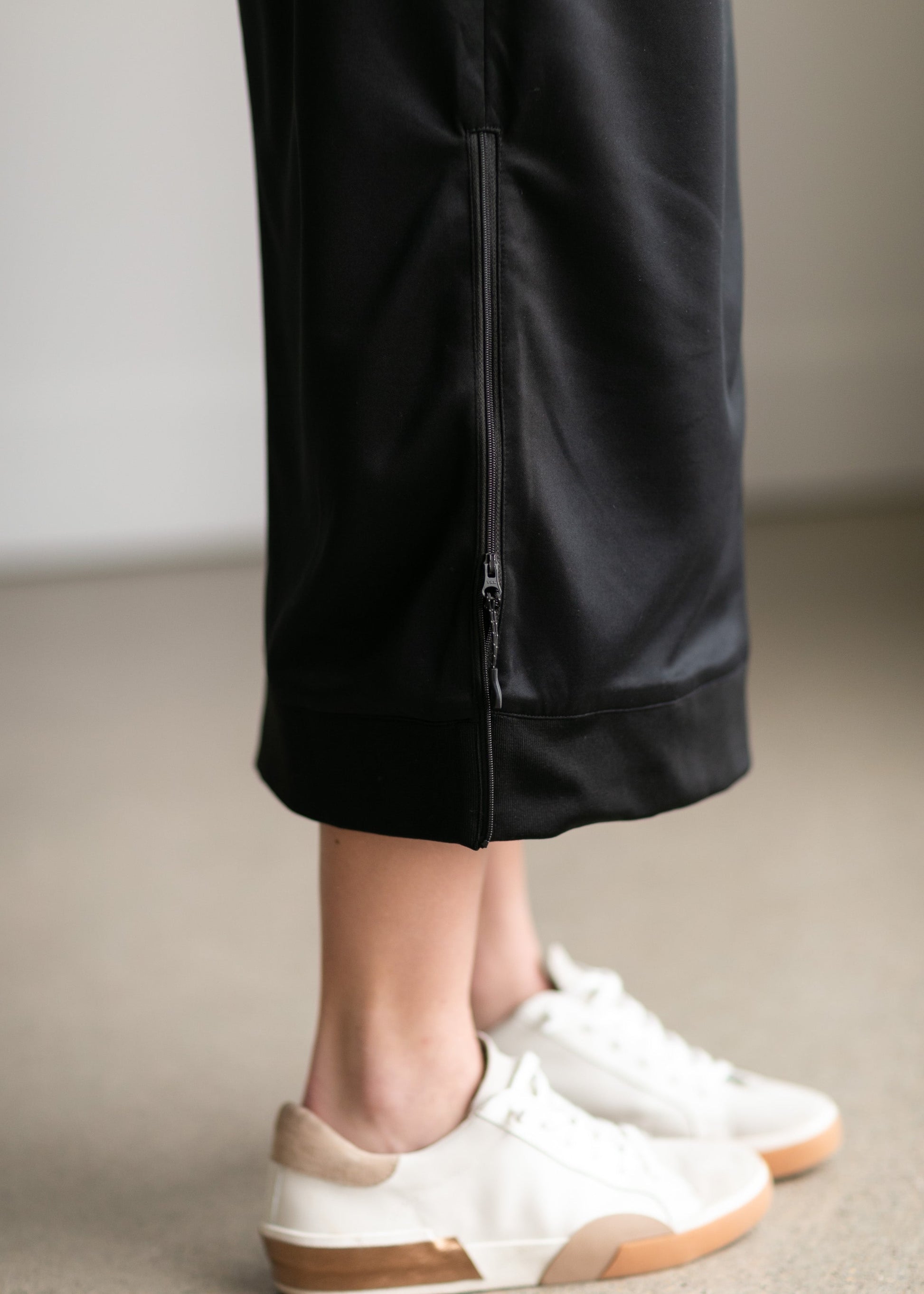 A black midi skirt with a drawstring waist, ribbed hem, pockets, and bottom side zipper.