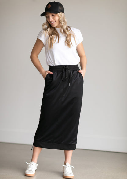 A black midi skirt with a drawstring waist, ribbed hem, pockets, and bottom side zipper.