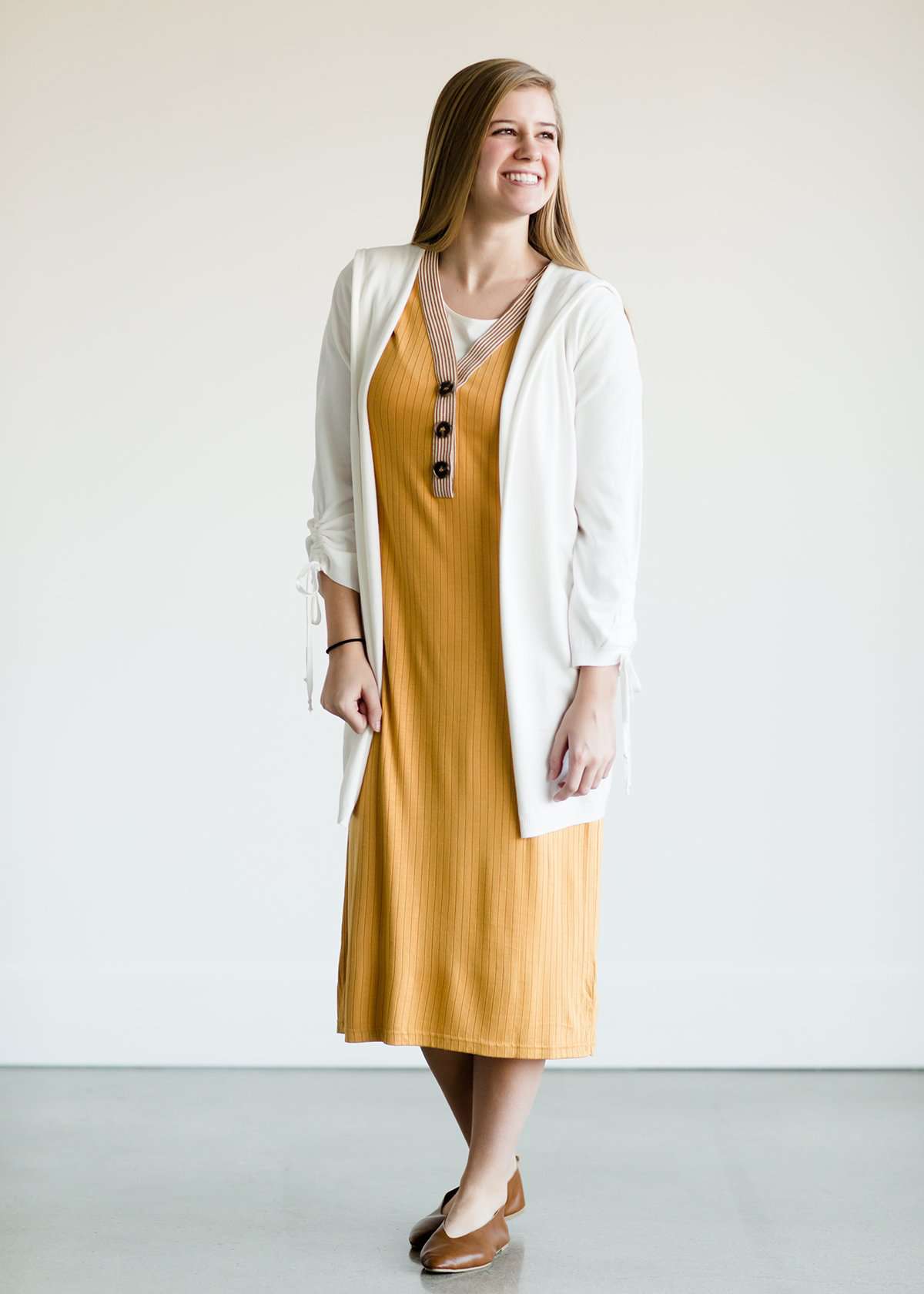 Woman wearing a ribbed mustard midi dress with faux wood buttons.