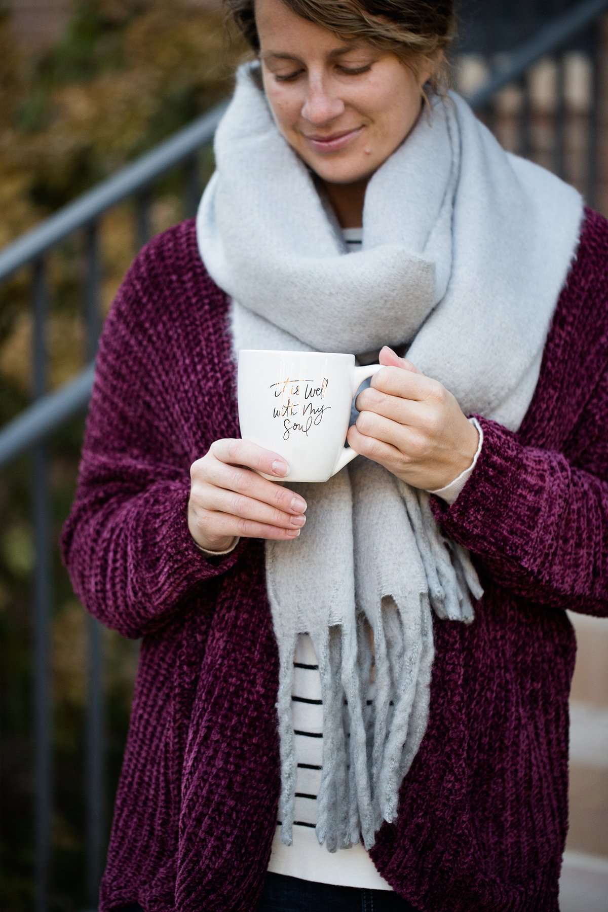 Woman wearing a gray fringe scarf that is super cozy and knit.