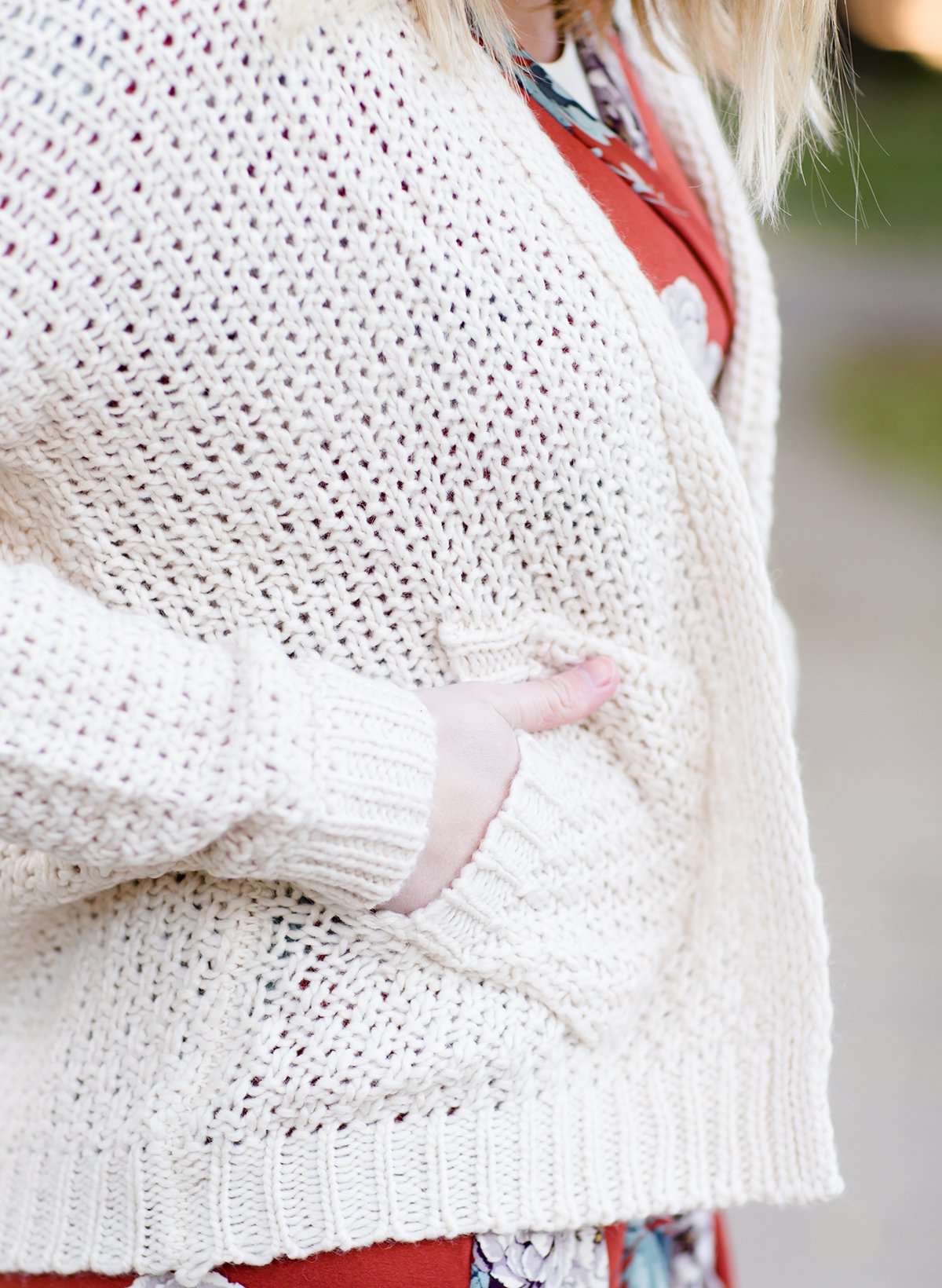 Young woman wearing a ivory chunky knit acrylic and wool sweater. This sweater has front pockets and features an open front.