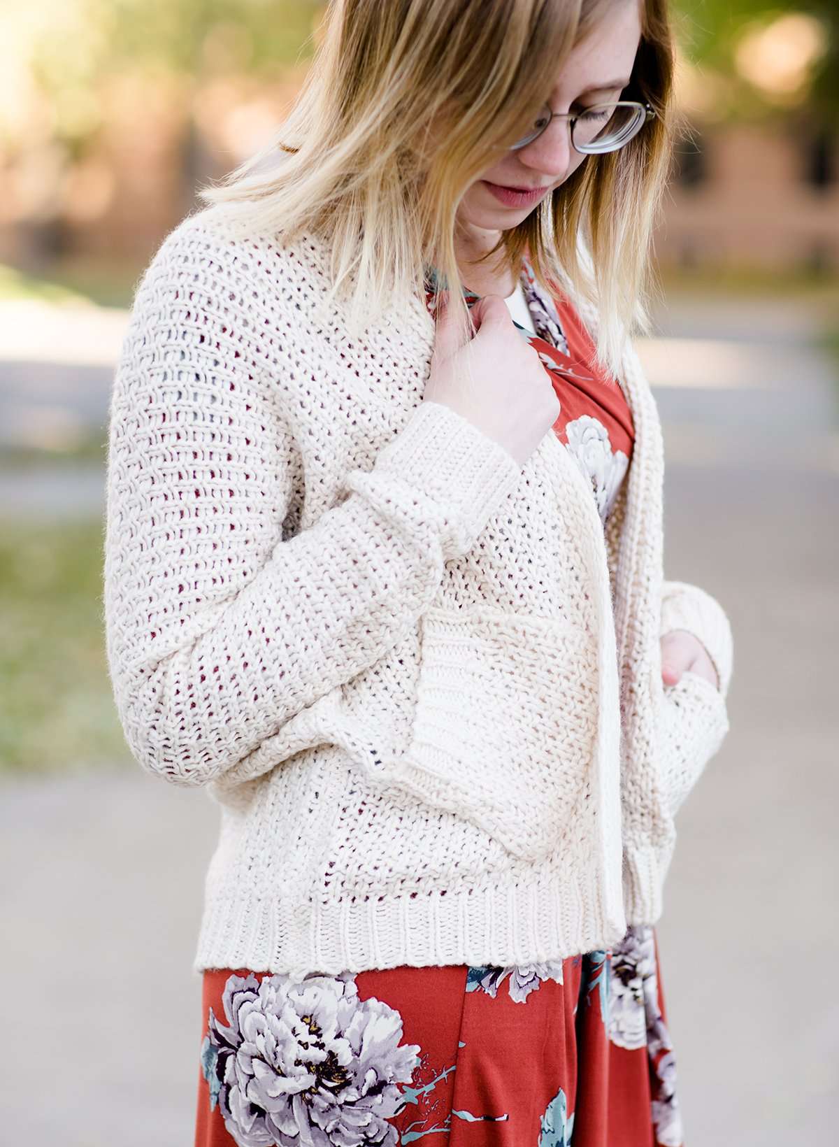 Young woman wearing a ivory chunky knit acrylic and wool sweater. This sweater has front pockets and features an open front.