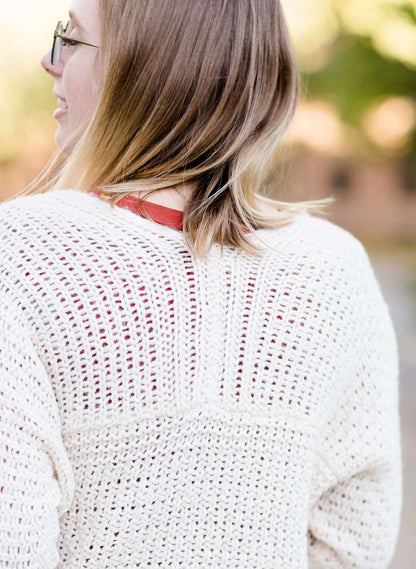 Young woman wearing a ivory chunky knit acrylic and wool sweater. This sweater has front pockets and features an open front.