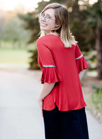 Woman wearing a rust colored, modest bell sleeve top. The 3/4 sleeves flutter and the top is also lined.