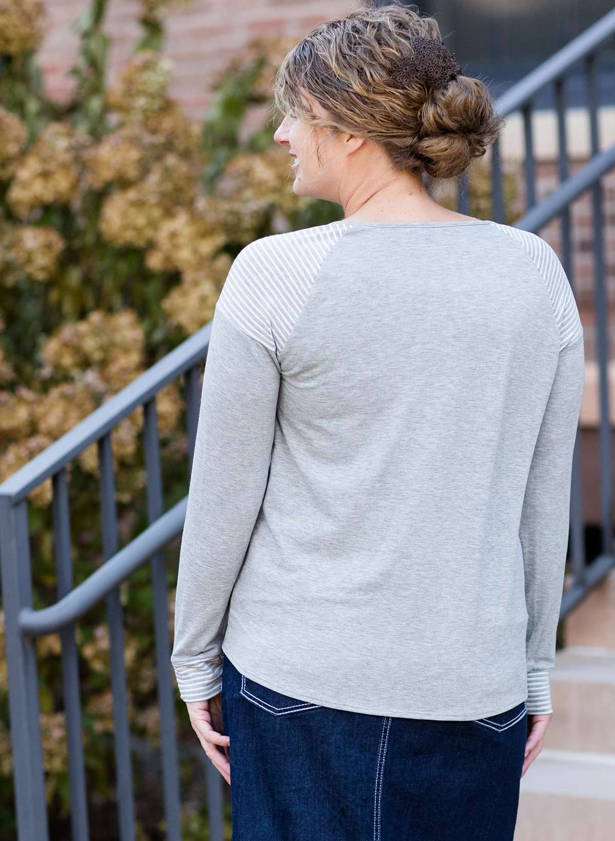 Woman wearing a gray tri blend top that has a striped pocket and a front tie.