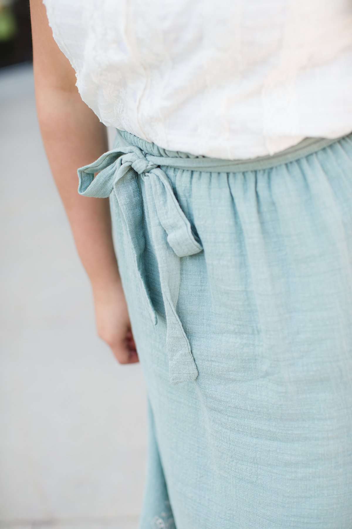 Woman wearing a mint green cotton midi skirt with a self tie and feminine crochet lace detail at the bottom hem