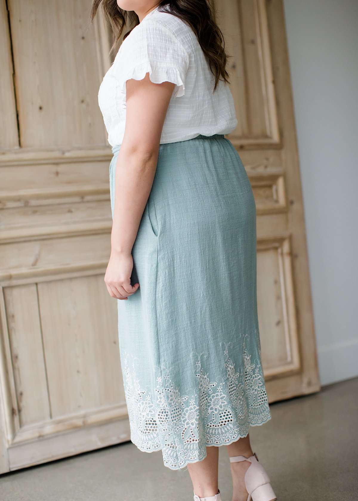 Woman wearing a mint green cotton midi skirt with a self tie and feminine crochet lace detail at the bottom hem