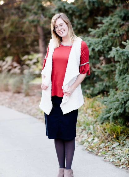 Young woman in a modest black midi skirt wearing a cream colored, soft drape style vest.