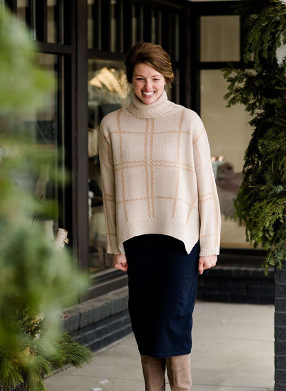 Woman wearing a shawl like sweater that is cream with a gold and orange subtle design.