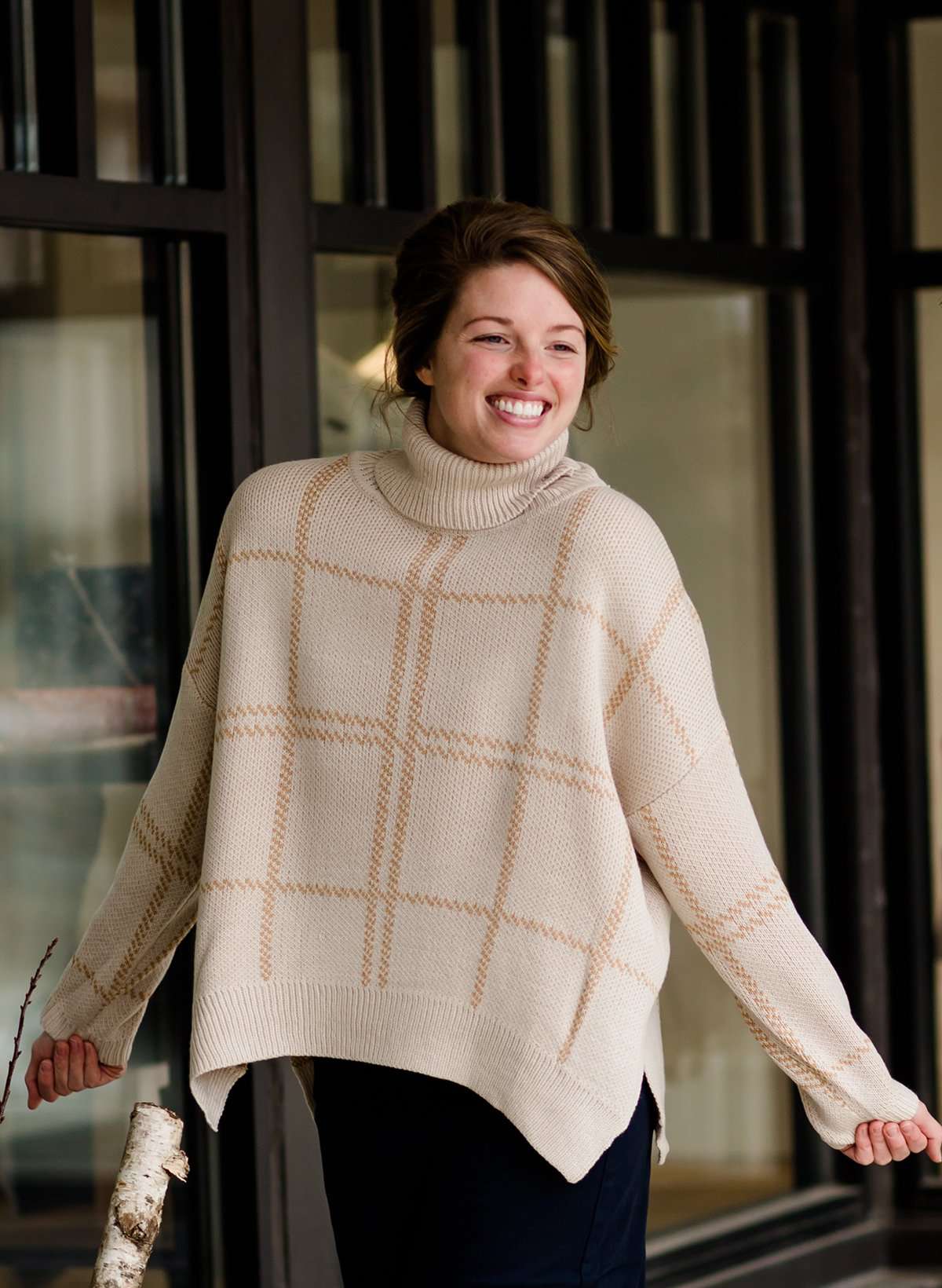 Woman wearing a shawl like sweater that is cream with a gold and orange subtle design.