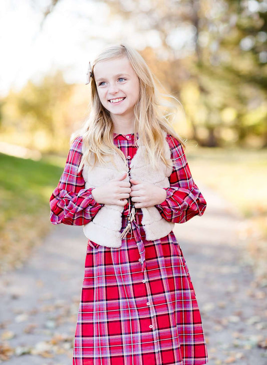 Young girl wearing a cream colored faux fur vest. It is a modest layering vest that also features beaded detail