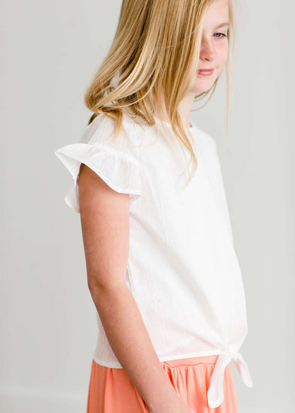 Girl wearing a modest ivory colored tie front top with flutter sleeves