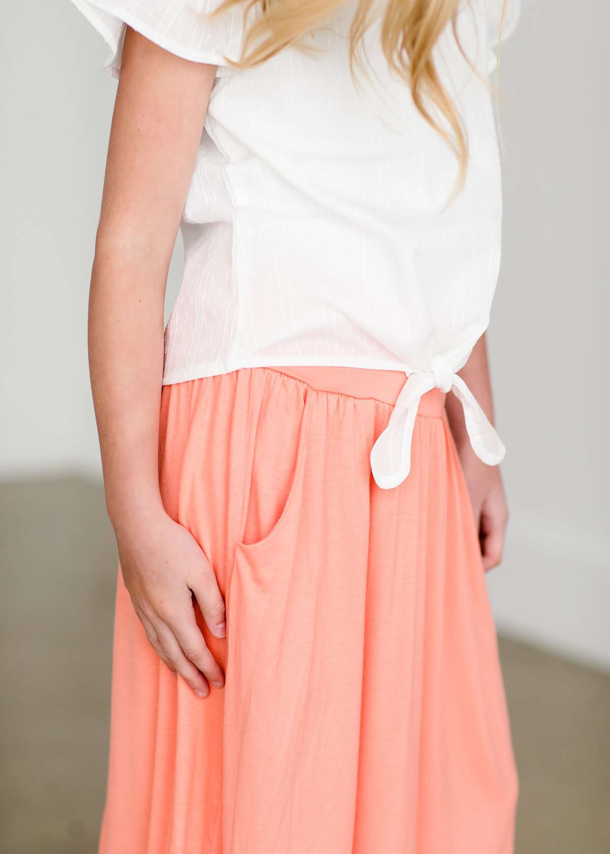 Girl wearing a modest ivory colored tie front top with flutter sleeves