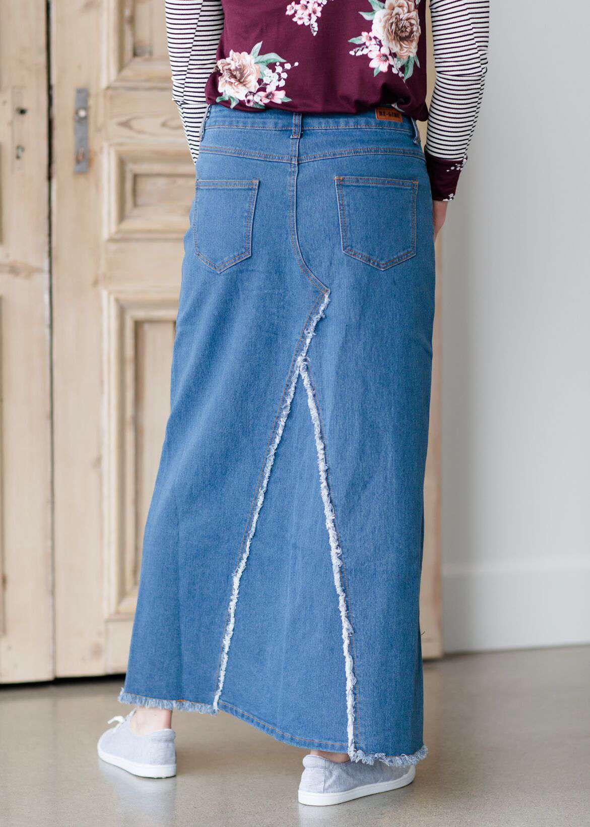 woman wearing an a-line modest long denim skirt with fringe detail and no slit