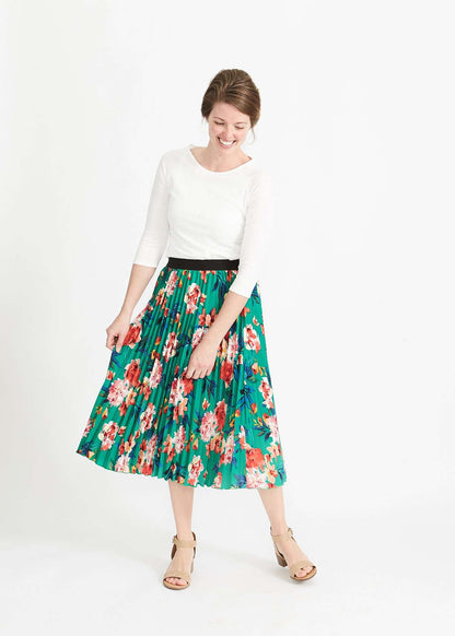 Woman wearing an emerald green floral stretchy pleated swing skirt with dress shoes and a white lace top