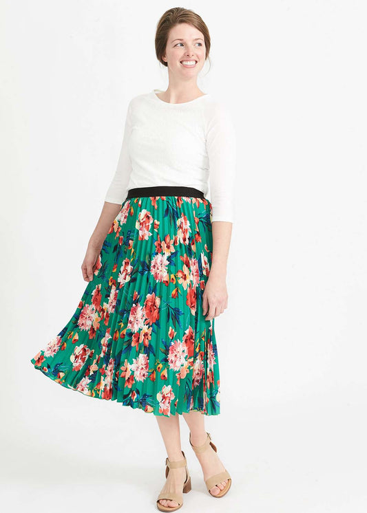 Woman wearing an emerald green floral stretchy pleated swing skirt with dress shoes and a white lace top