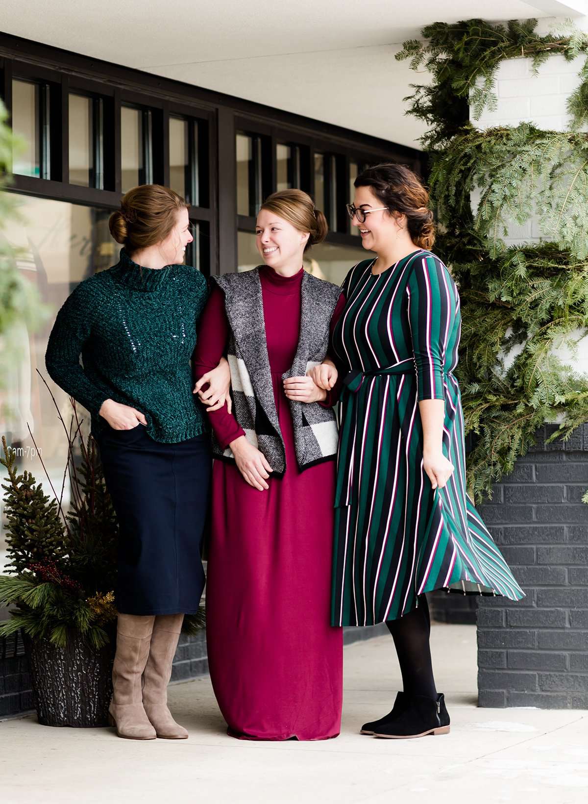 Modest woman wearing a green and black striped midi dress with a self tie bow. She is wearing black leggings and black booties as well. She is at Inherit Clothing Company.