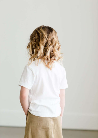 Toddler girl wearing a white minnesota logo on a white tee shirt. She is also wearing a long khaki skirt.