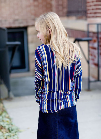 Young girl wearing a multi colored striped dolman top with a front tie. Colors in this top are navy, yellow, red, purple, green and white!