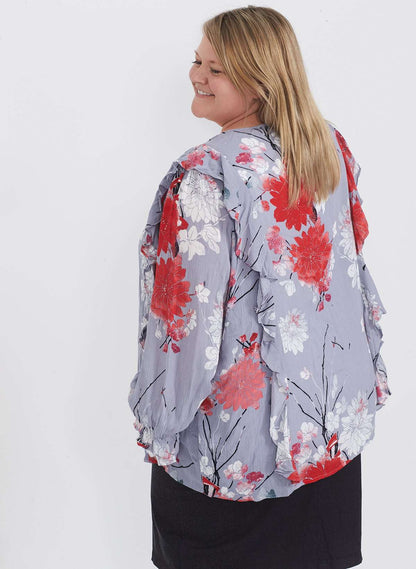 Plus size woman wearing a ruffle and floral gray blouse. This blouse has a key hole back and long sleeves. 