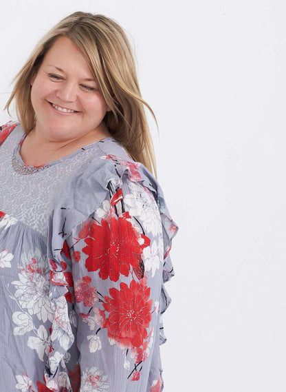 Plus size woman wearing a ruffle and floral gray blouse. This blouse has a key hole back and long sleeves. 