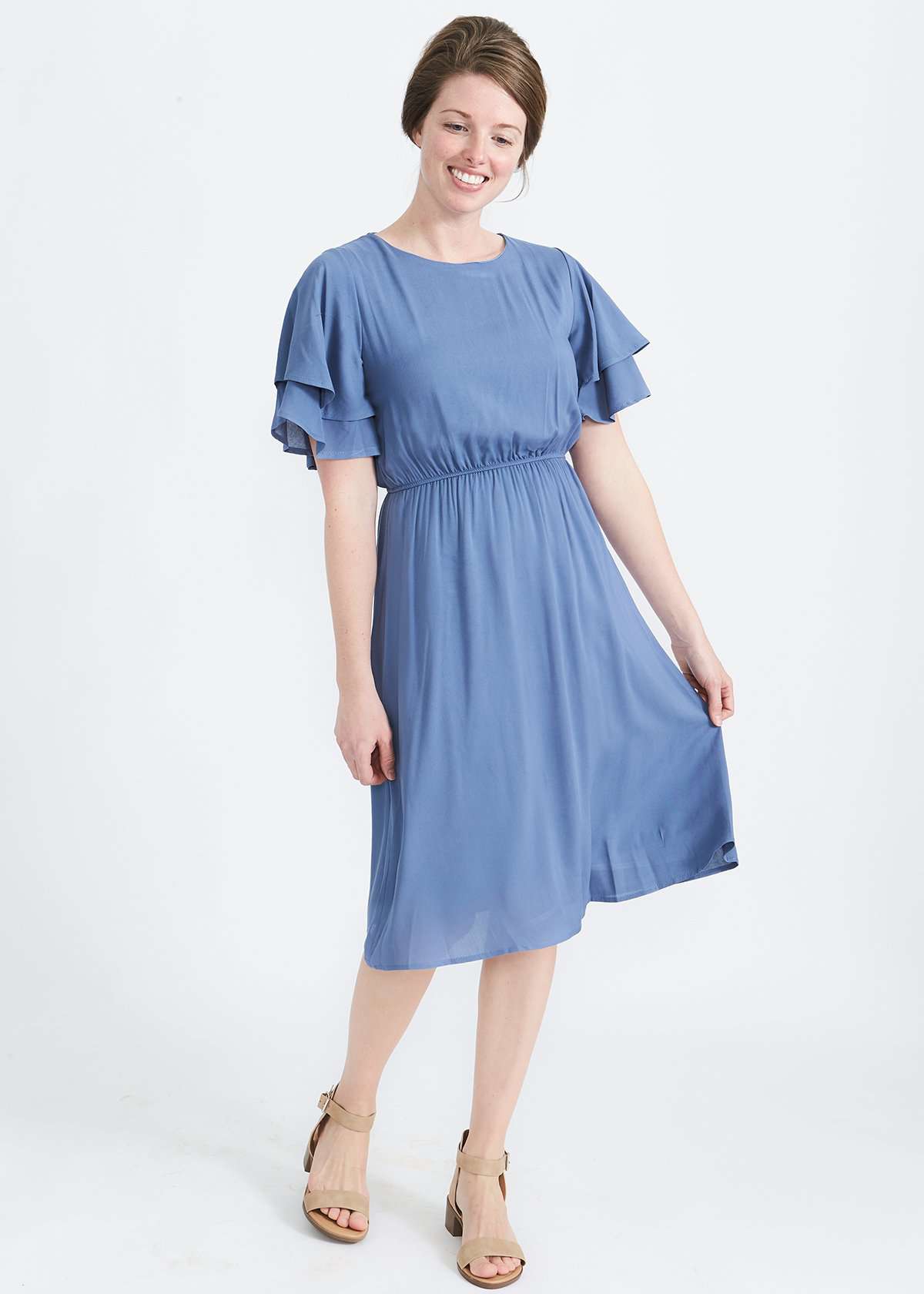 woman wearing a dusty blue empire waist dress with double ruffle sleeves that is lined and falls below the knee