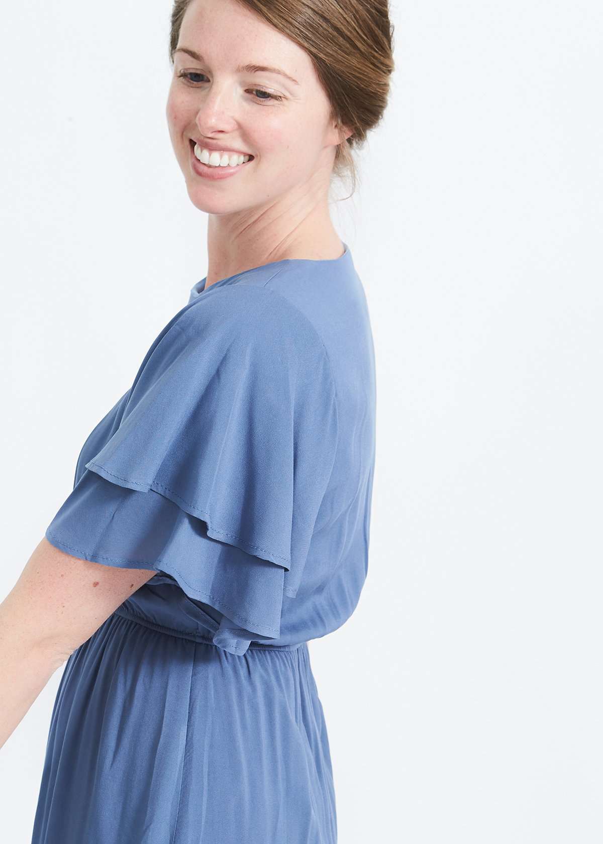 woman wearing a dusty blue empire waist dress with double ruffle sleeves that is lined and falls below the knee