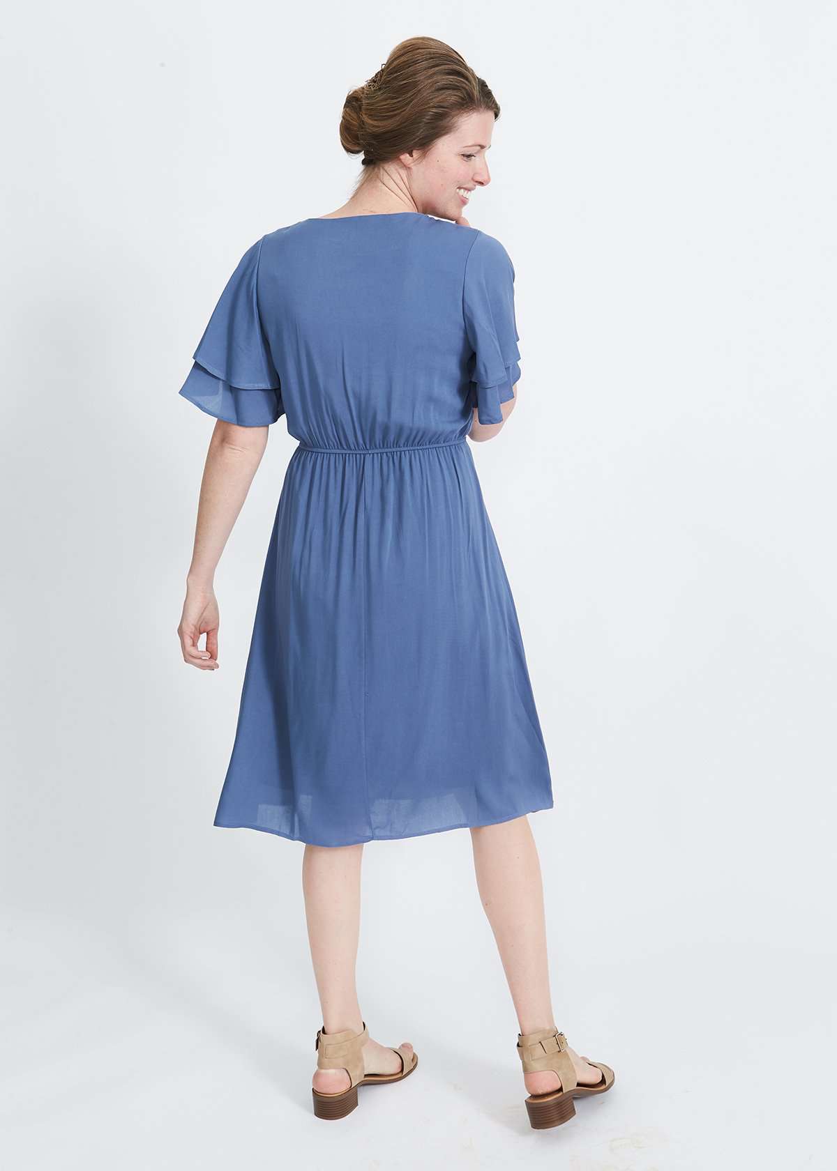 woman wearing a dusty blue empire waist dress with double ruffle sleeves that is lined and falls below the knee